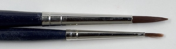 Close-up of two synthetic round watercolour brushes in different sizes, showing their pointed tips and round ferrules