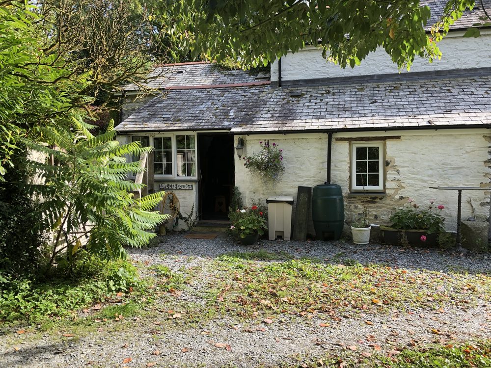 White rendered Devon cottage with a slate roof seen close up from the drive