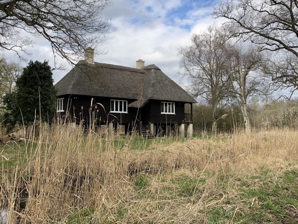 Dark boarded fen bungalow raised on stilts under a deep thatched roof