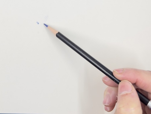 Hand demonstrating holding a coloured pencil further back from the tip to achieve lighter pressure and broader strokes.
