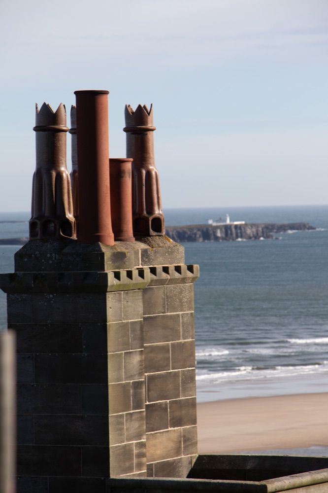 Ornate terracotta and crown-topped chimney pots on a stone stack at Bamburgh Castle, with the Farne Islands out at sea beyond