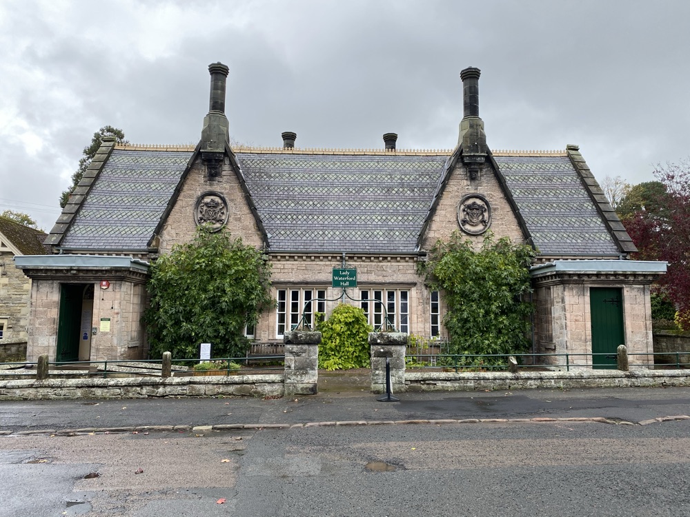 Two tall ornate stone chimney stacks rising upright from a patterned tiled roof on a stone hall