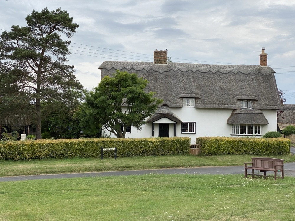 White thatched cottage with a decorative scalloped ridge line along the crown of the roof and two brick chimneys