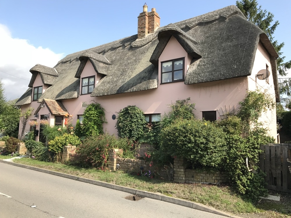 Pink-washed thatched cottage with a brick chimney, built in 1622, in an English village