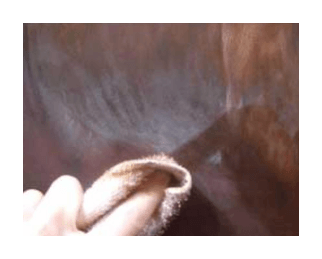 A hand gently wiping away the hazy residue of wax bloom from a dark coloured pencil artwork using a soft cloth.