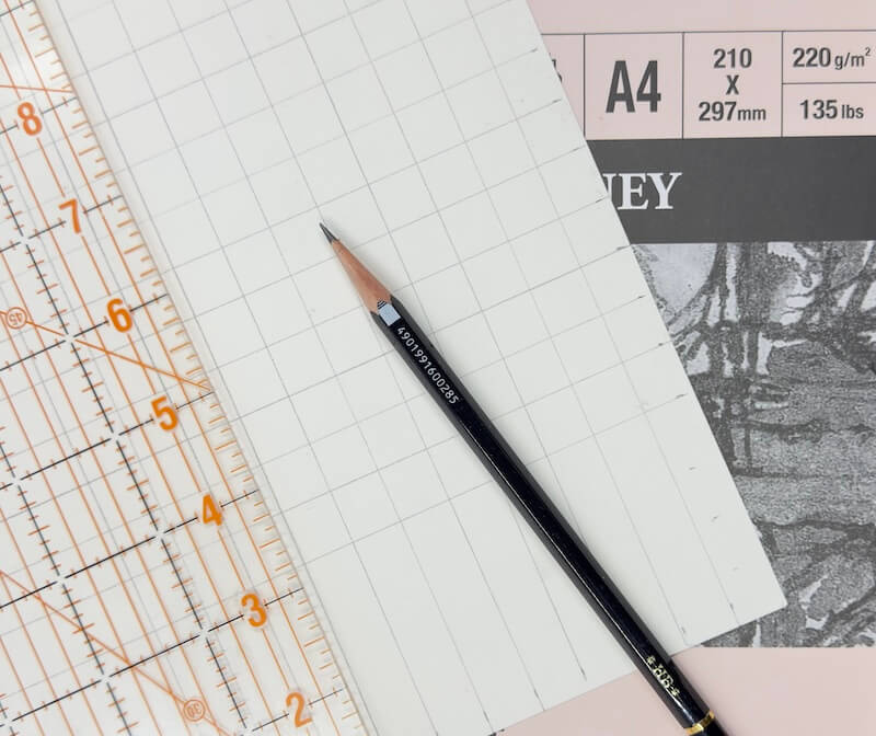 Preparing drawing paper for the grid method: Using a sharp graphite pencil and clear ruler to mark out light grid lines on heavyweight paper