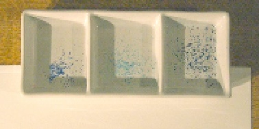 A white artist's palette with three mixing wells, each containing a small pile of dry, shaved blue watercolour pencil pigment.