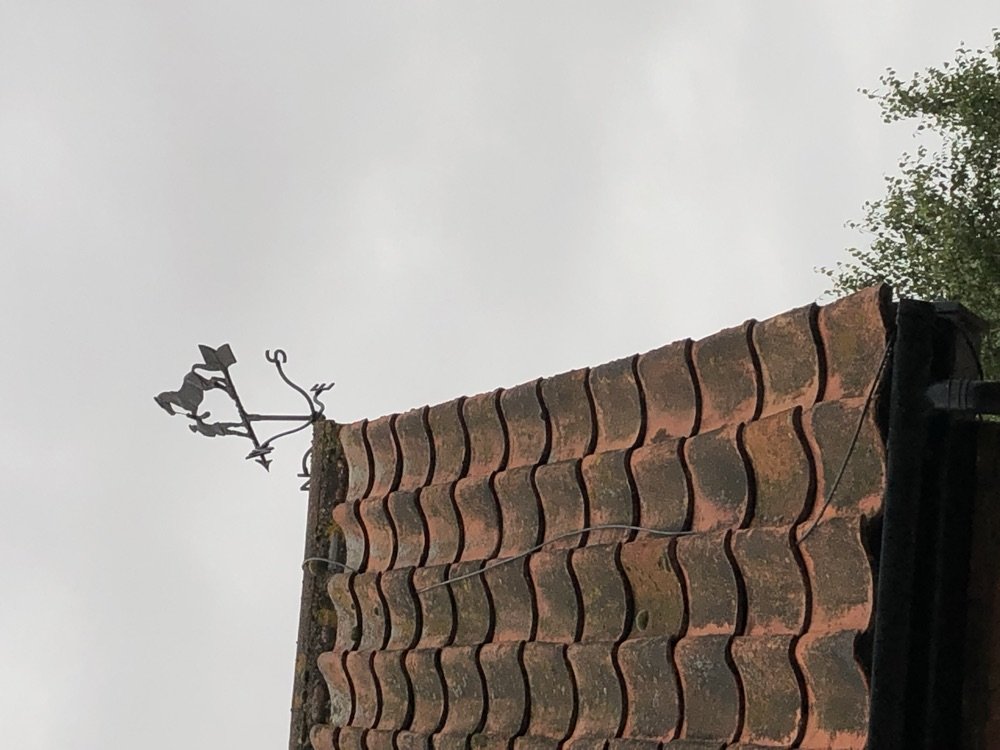 Close-up of curved S-shaped clay pantiles on a roof ridge with an ornate iron weather vane