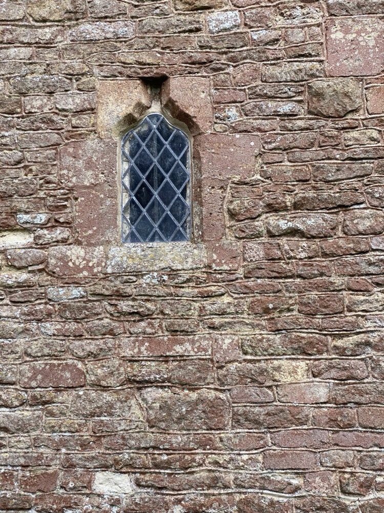 Coursed red sandstone church wall around a leaded Gothic window